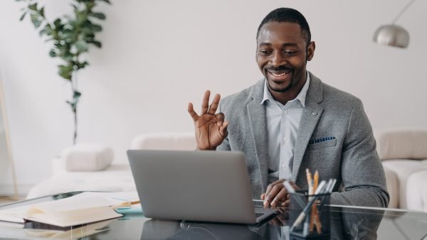 Smiling african american man talk by video call using laptop app agree with coworker, showing ok sign. Friendly black businessman freelancer show okay gesture to client, working online at distant job.