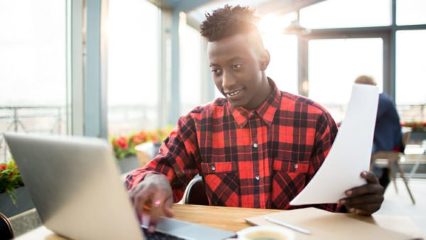 African-american guy in shirt sitting in cafe in front of laptop and preparing report for conference or watching webinar