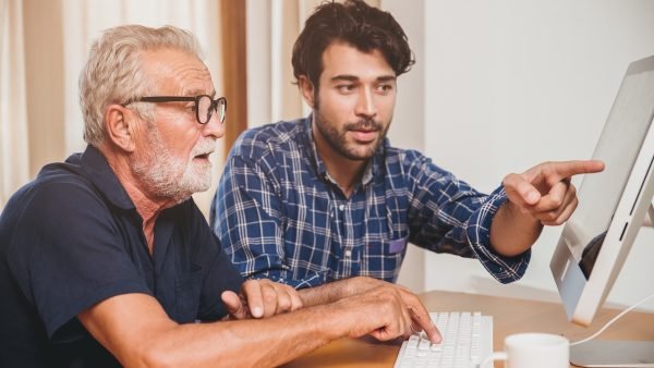 young man or son teaching his grandfathe elderly dad learning to using computer at home.
